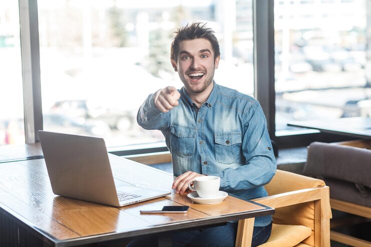 hey-you-portrait-happy-positive-bearded-young-freelancer-blue-jeans-shirt-are-sitting-cafe-working-laptop-with-toothy-smile-pointing-finger-you-looking-camera-indoor_416530-10708