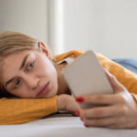 Woman lying on bed while scrolling through social media on phone